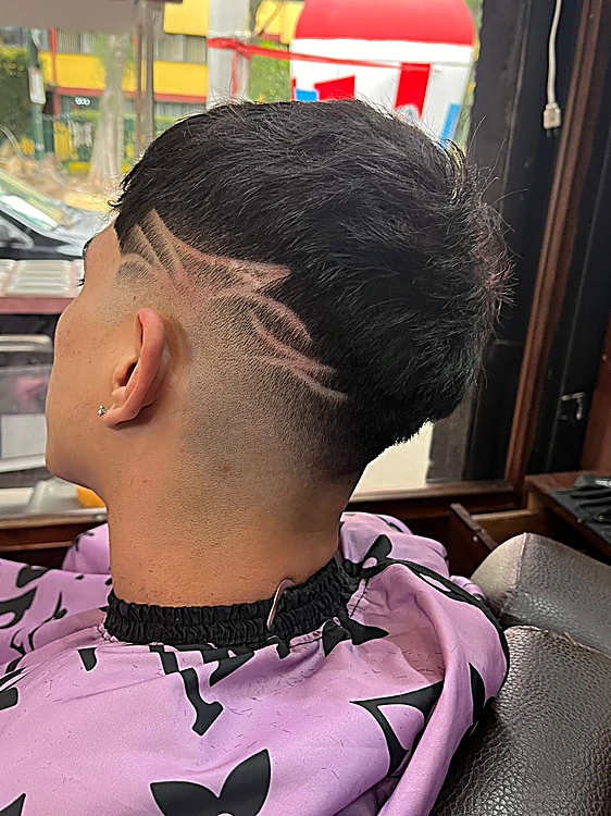 Corte con fade bajo y diseño de rayas rasuradas en un costado de la cabeza, visto de espaldas.