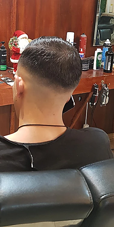 Nuca con fade limpio de un cliente sentado en el sillón, frente al tocador de madera.