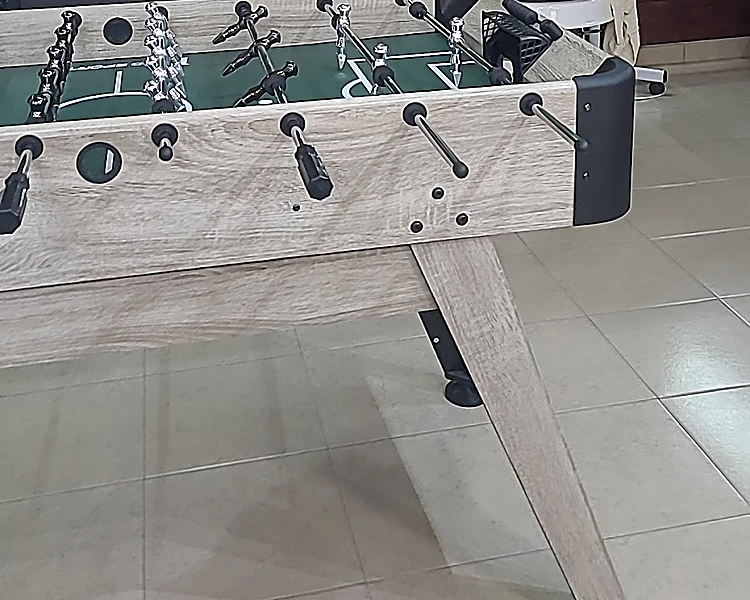 Futbolito de madera clara con cancha verde y jugadores en sus varillas, en la sala de espera.