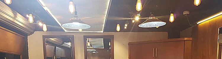 Techo del salón con lámparas colgantes, focos cálidos, espejos con marco de madera y paneles de madera rojiza.